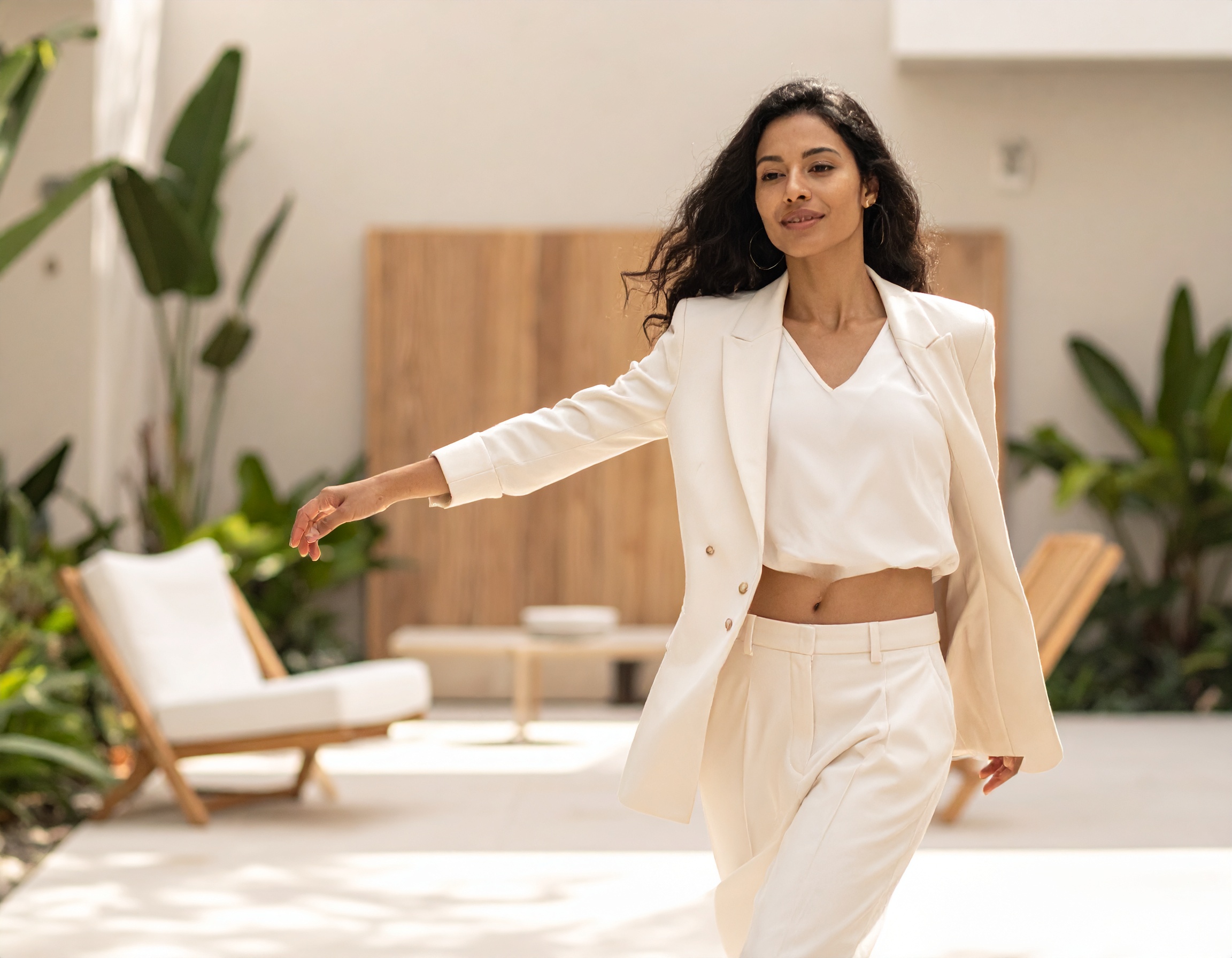 A woman in a cream suit walking a courtyard, one arm swung open