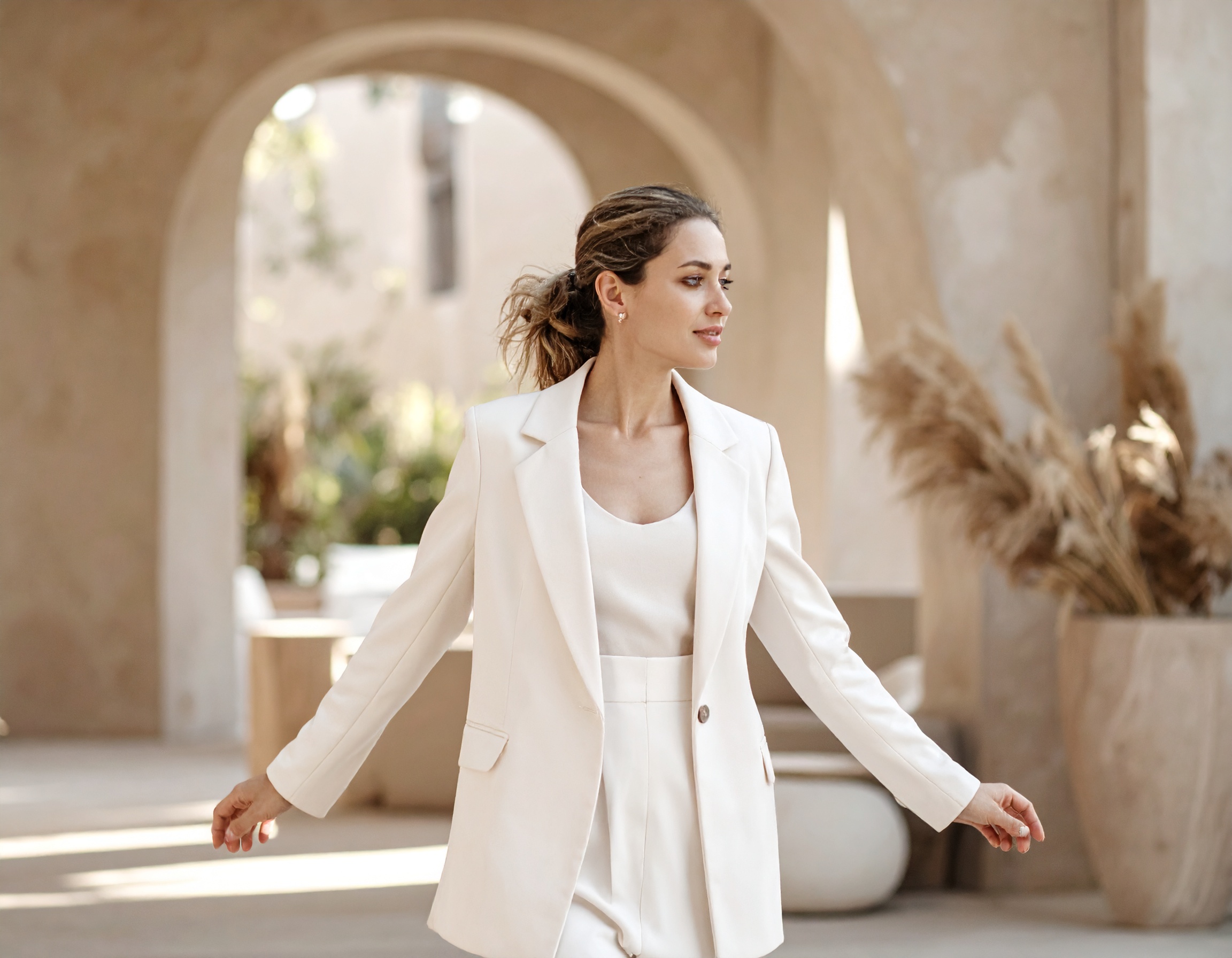 A woman in a cream suit, arms open, standing under a plaster arch