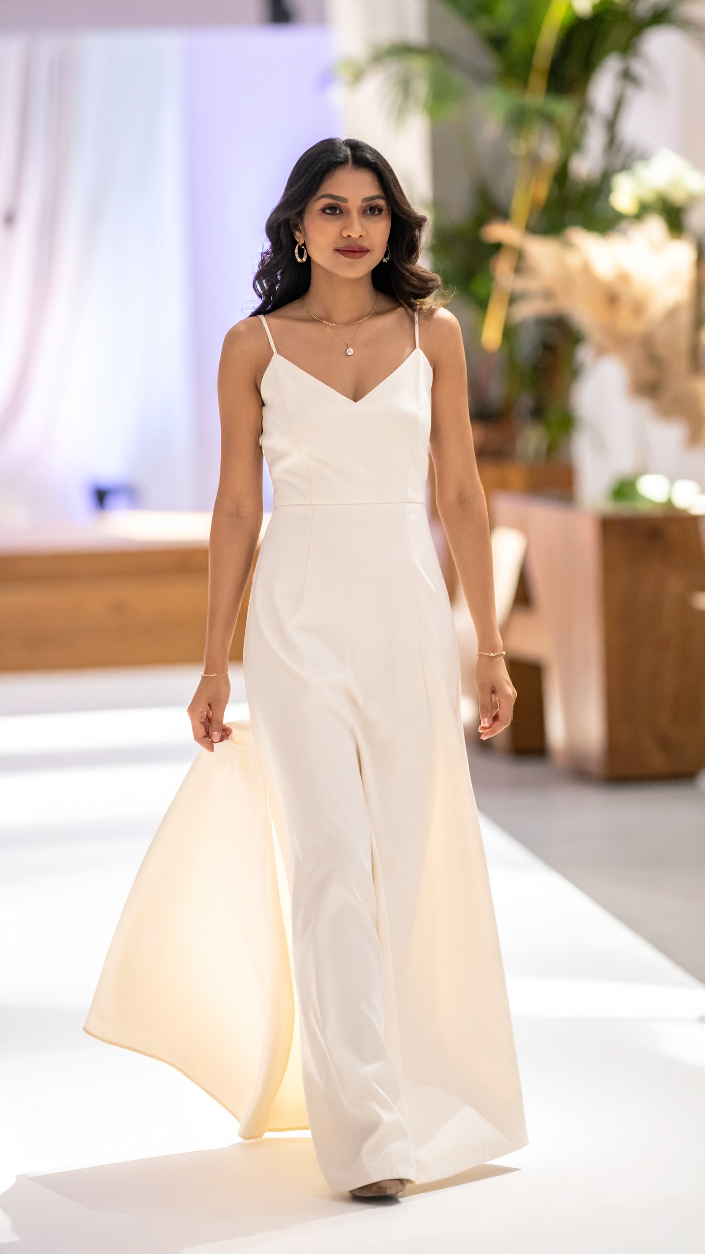 A woman in a white gown carrying the weight of her own skirt across a lit floor