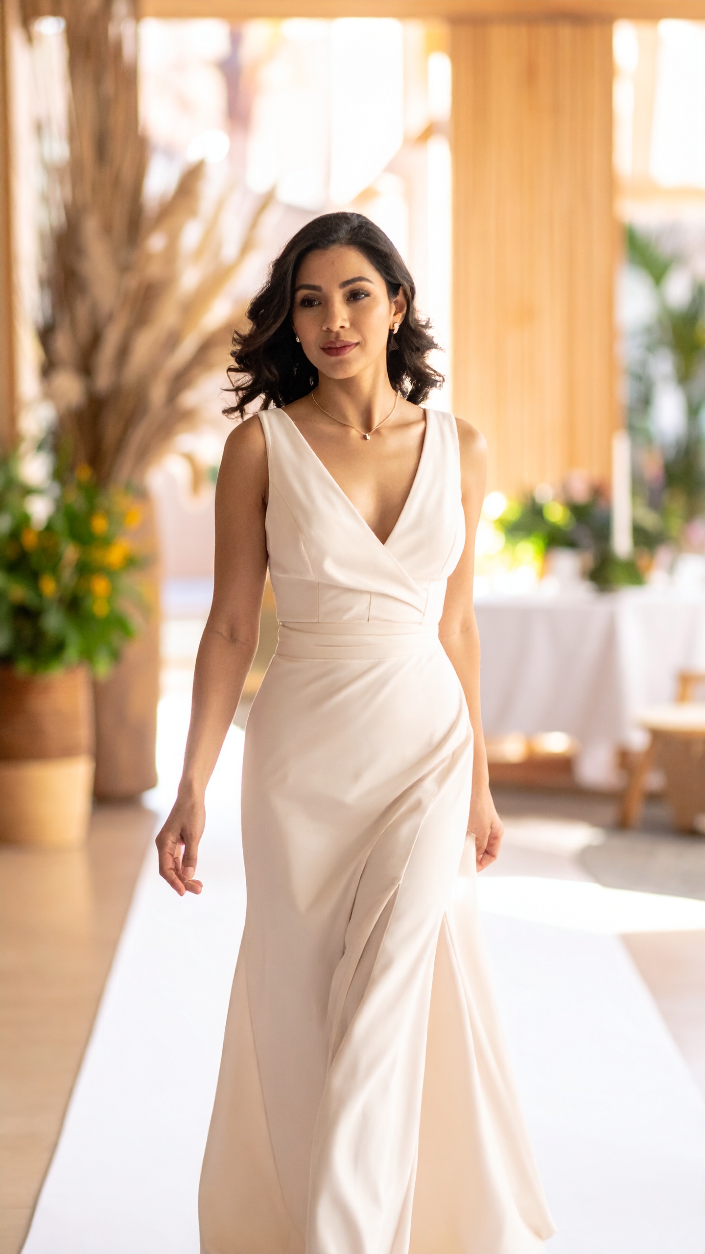 A woman in a deep-V gown crossing a warm room hung with light