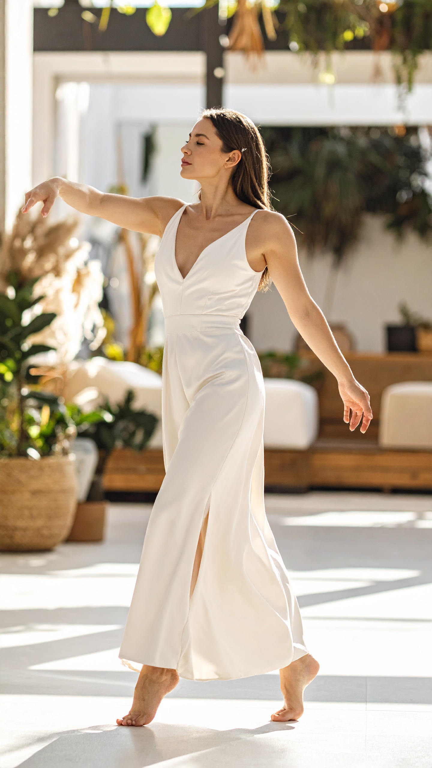 A woman in a pale gown turning barefoot, skirt lifting, bright terrace behind her