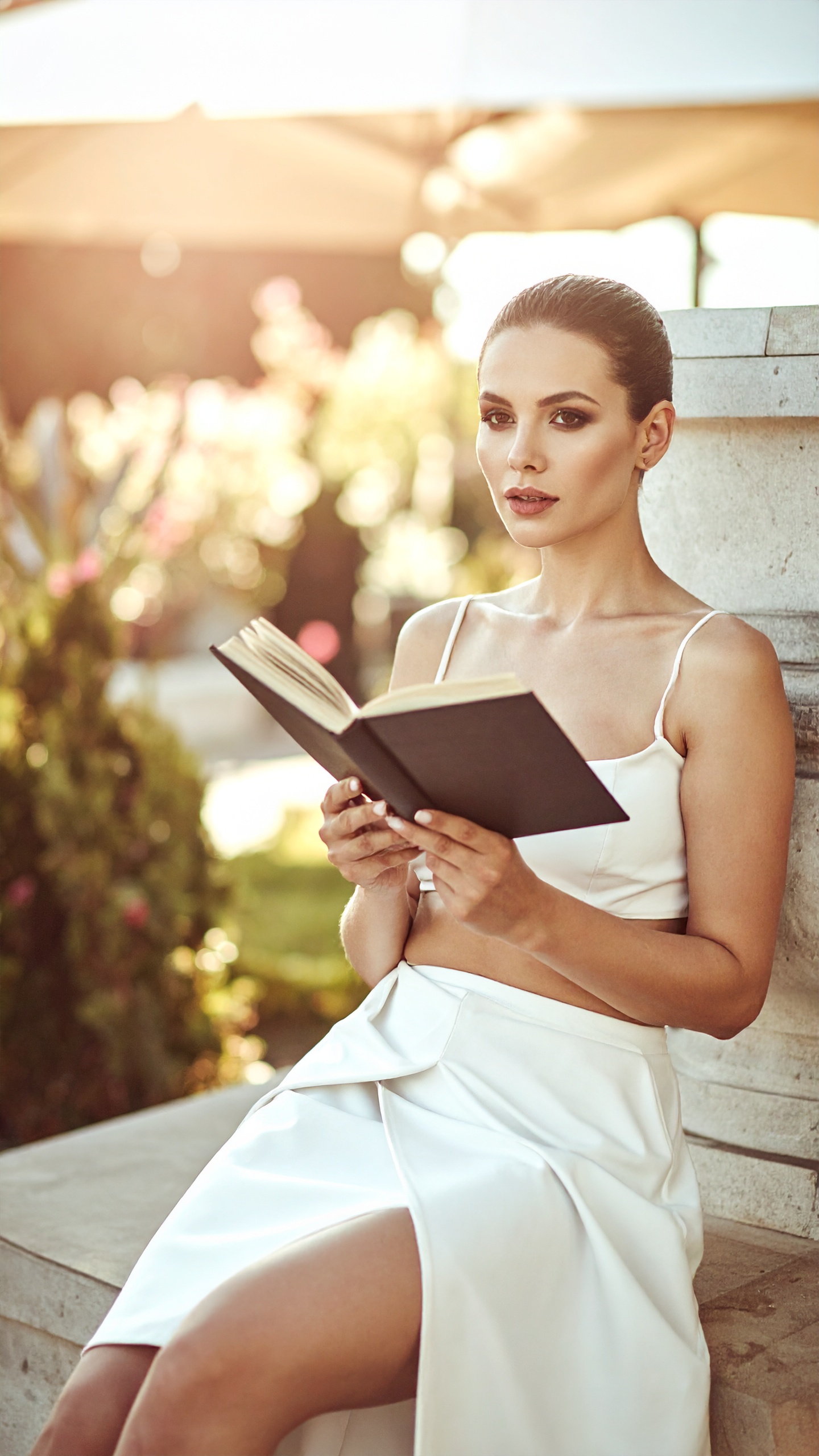 A woman in a pale gown seated in warm light, reading