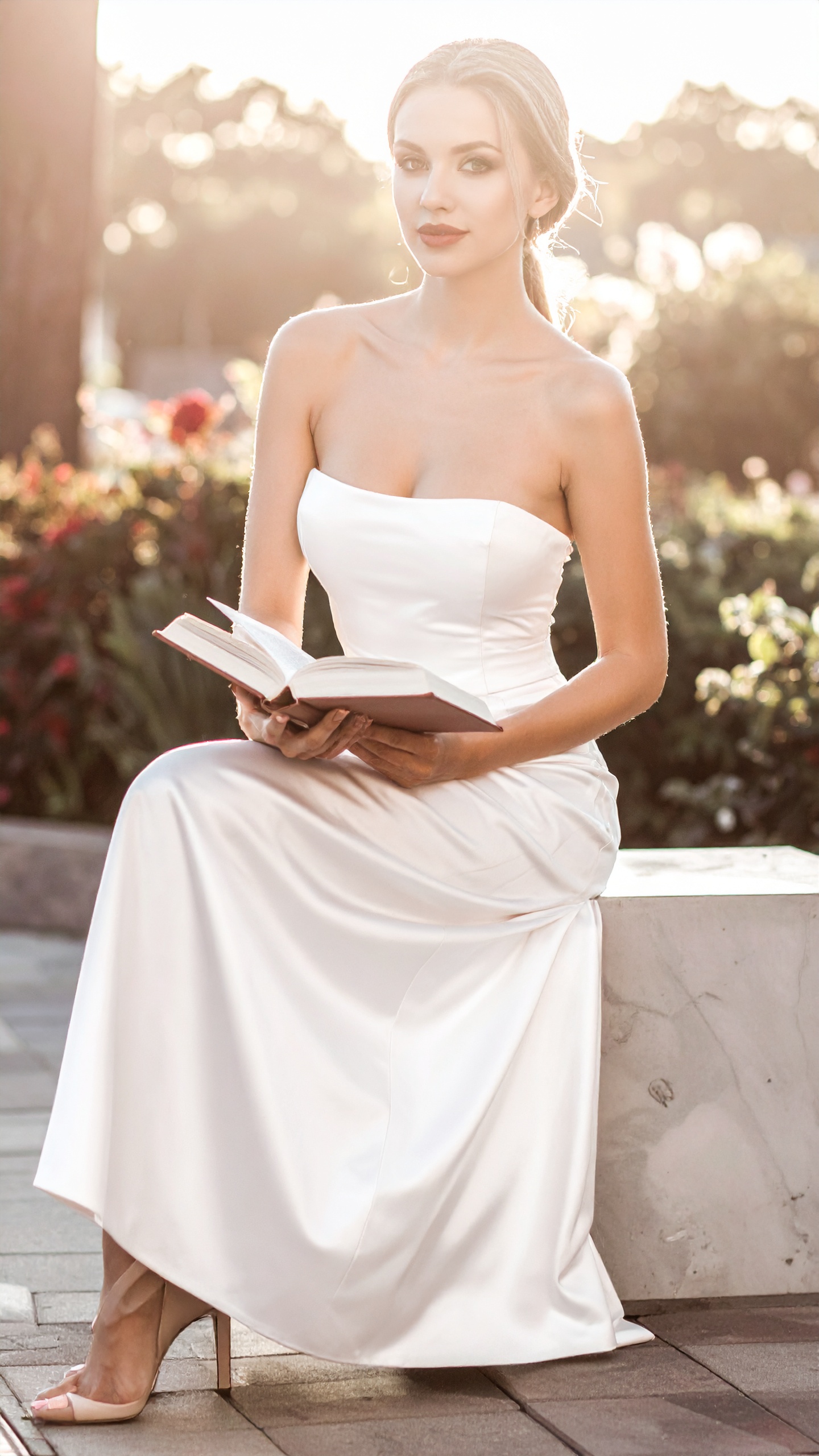 A woman in a pale gown seated in low golden light, an open book in her hands